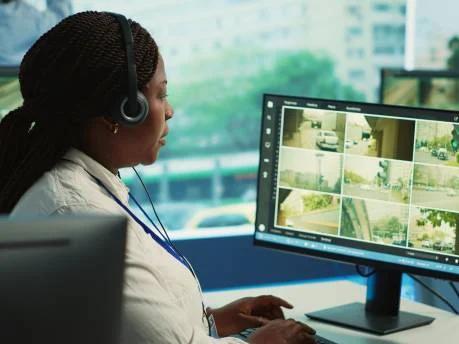 An operator watching a multi-camera CCTV grid from a control desk