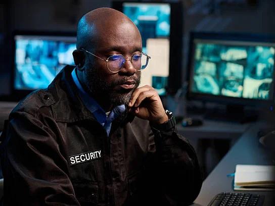 A security officer reviewing camera feeds on screens overnight
